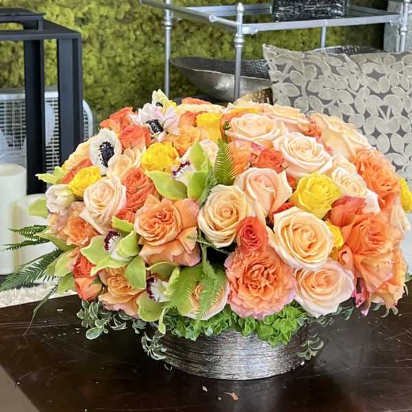 Low floral arrangement of peach, pink, and yellow roses in a silver bowl
