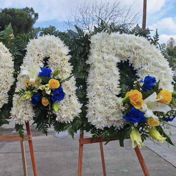 Three large white floral wreaths on wooden easels with blue and yellow roses