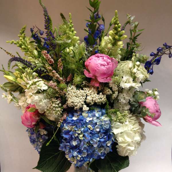 Tall mixed bouquet with blue hydrangeas, pink peonies, and white blooms in a glass vase