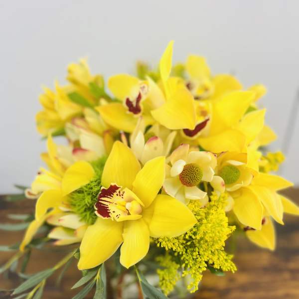 Yellow orchid bouquet with green filler in a glass vase