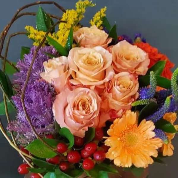 Colorful arrangement of peach roses, orange gerbera, and mixed blooms in a low container