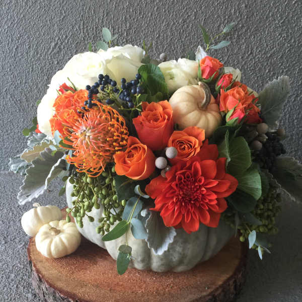 Orange and white floral arrangement in a pumpkin centerpiece with small pumpkins