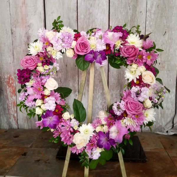 Heart-shaped floral wreath with pink, white, and purple flowers on a stand
