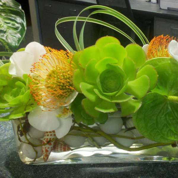 Green and white floral arrangement in a rectangular glass vase