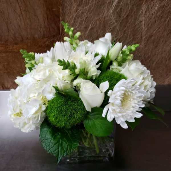 White floral arrangement in a clear square vase with green accents