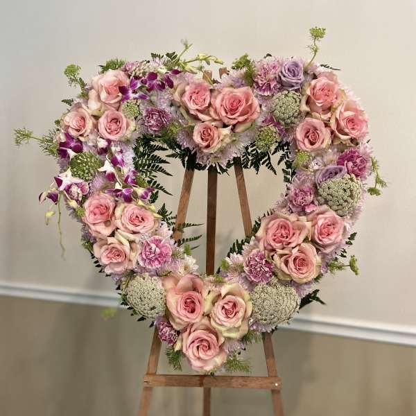Heart-shaped floral wreath with pink roses and lavender blooms on a wooden easel