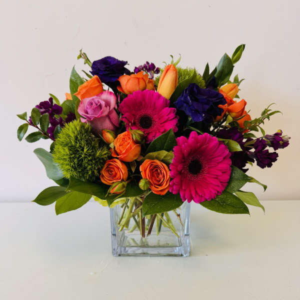 Mixed bouquet of pink gerberas, orange and purple roses in a glass vase