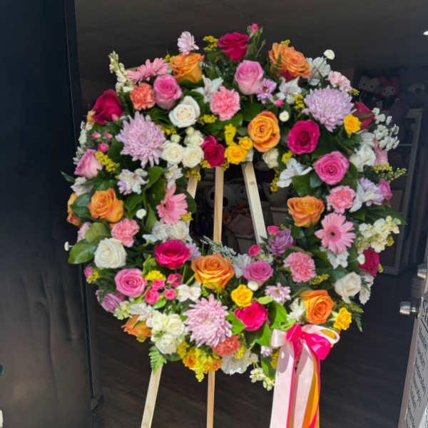 Large floral wreath on a wooden easel with pink, orange, white, and yellow blooms
