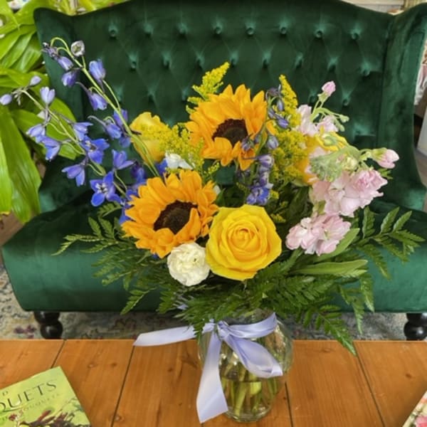 Bouquet of sunflowers, yellow roses, and blue flowers in a glass vase