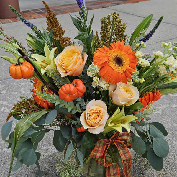 Autumn bouquet with orange gerbera daisies, peach roses, and small pumpkins in a glass vase