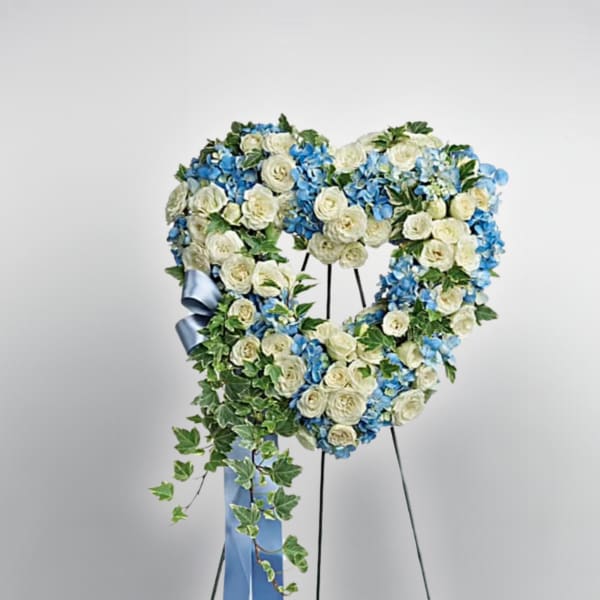 Heart-shaped floral wreath of white and blue flowers on a stand with a blue ribbon