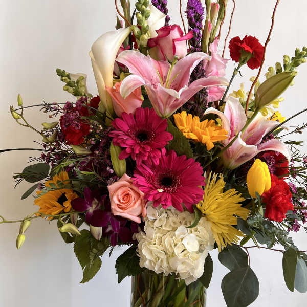 Mixed bouquet in a tall glass vase with lilies, gerberas, roses, and hydrangea