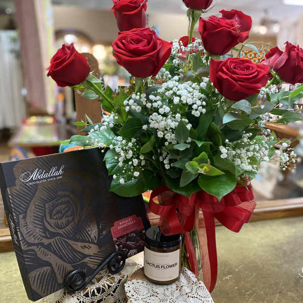 Red roses arranged with baby's breath, a chocolate box, and a candle