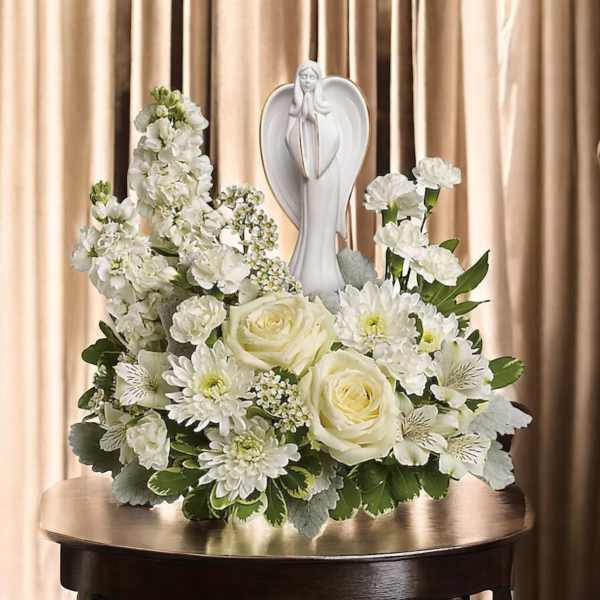 White floral arrangement with roses and daisies around a praying angel statue