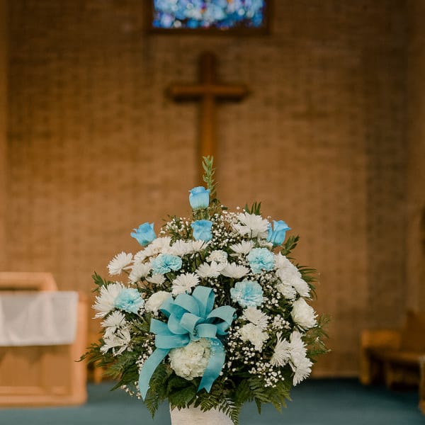White and blue funeral arrangement in a white urn with a ribbon bow