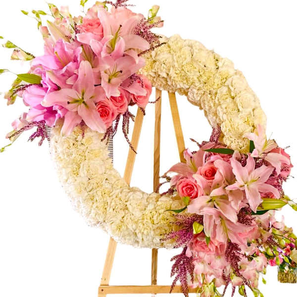 Floral wreath on an easel with pink lilies, roses, and cream flowers