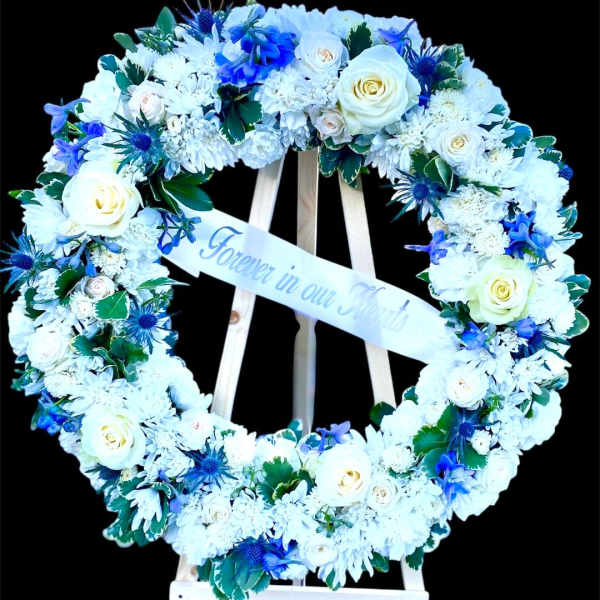 Heart-shaped floral wreath with white and blue flowers on a stand
