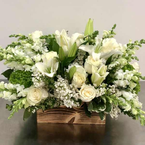 White floral arrangement in a wooden box with lilies, roses, and snapdragons