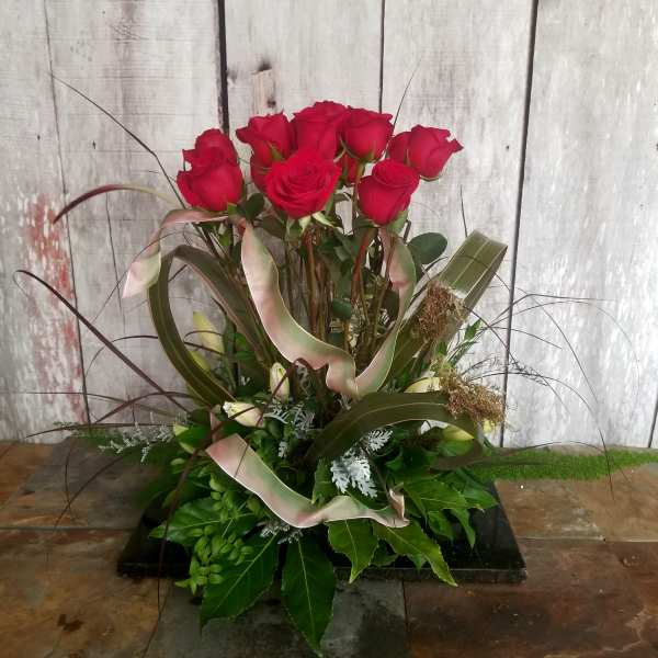 Tall arrangement of red roses with decorative ribbon and foliage
