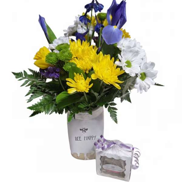 Mixed yellow, white, and blue flowers in a white container with a small gift box