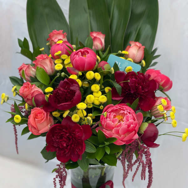 Pink and burgundy flowers arranged in a glass vase with a ribbon