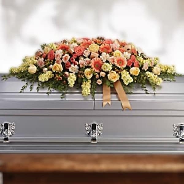Peach and yellow casket spray of roses and mixed blooms with ribbon on a silver casket