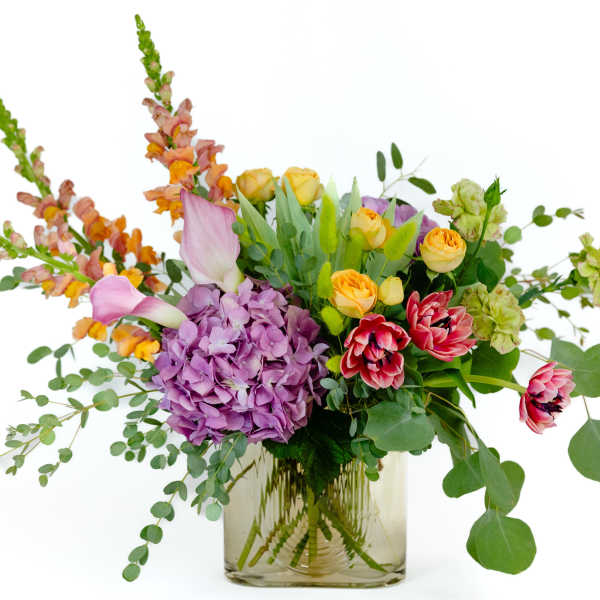 Mixed bouquet with purple hydrangea, yellow roses, and pink tulips in a glass vase