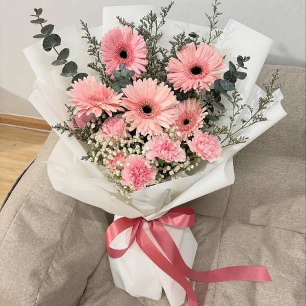 Pink gerbera daisy bouquet wrapped in white paper with a pink ribbon