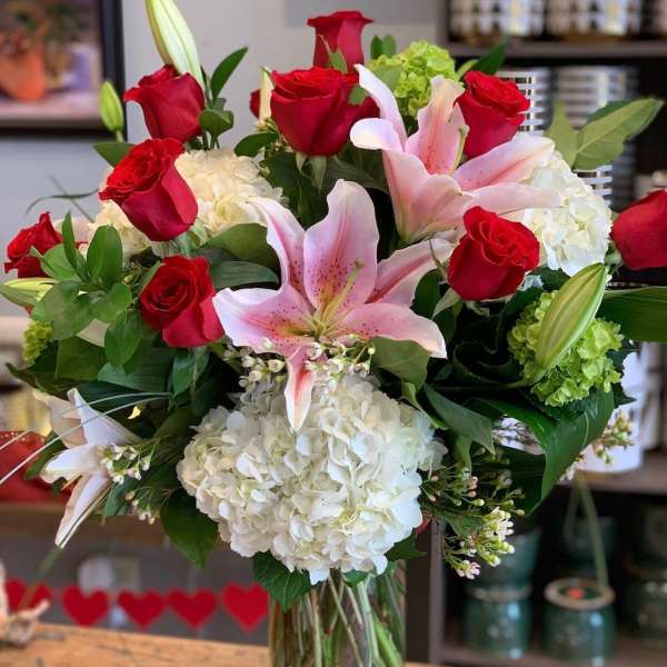 Vase arrangement of red roses, pink lilies, and white hydrangeas in a clear glass cylinder