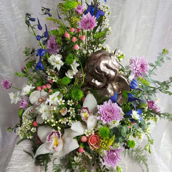 Tall floral arrangement with blue and pink flowers and a metallic angel figure