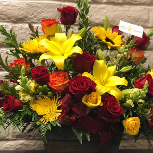 Bouquet of red and yellow roses with lilies and sunflowers in a black vase