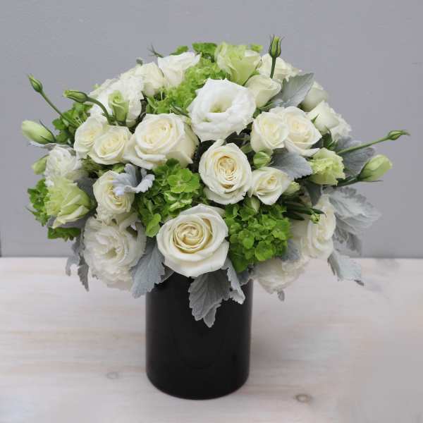 Compact arrangement of white roses and lisianthus with green blooms in a black cylinder vase