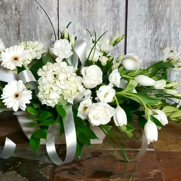 White floral arrangement with daisies, roses, and ribbon in a low container