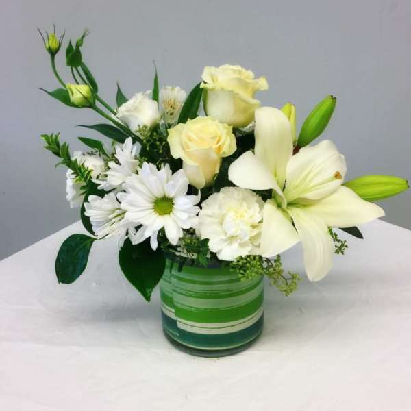 White lilies, roses, and daisies arranged in a green glass vase