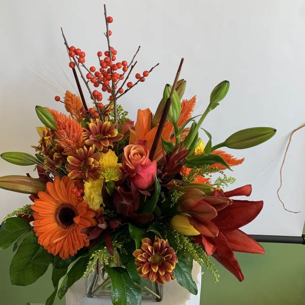 Autumn bouquet with orange gerbera daisies, lilies, and red berries in a vase