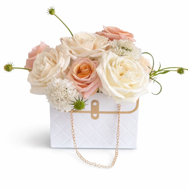 Cream and blush roses arranged in a white handbag-style box