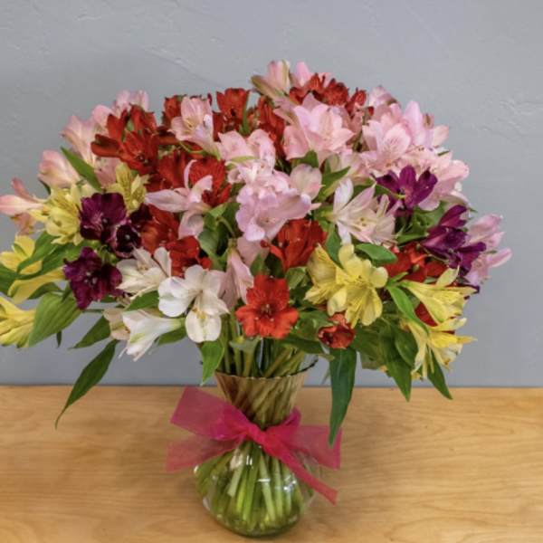 Mixed bouquet of colorful alstroemeria in a glass vase with a pink ribbon