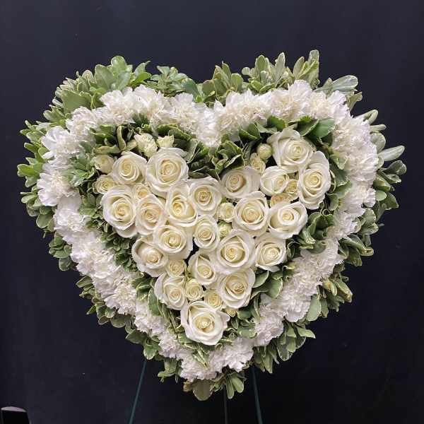 Heart-shaped white rose and carnation funeral spray on a stand