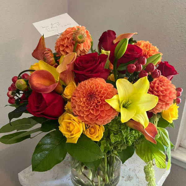 Mixed bouquet of red, orange, and yellow flowers in a clear glass vase