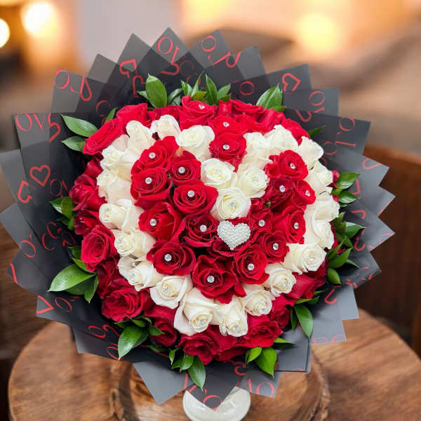 Red and white rose bouquet in black wrap with a white vase