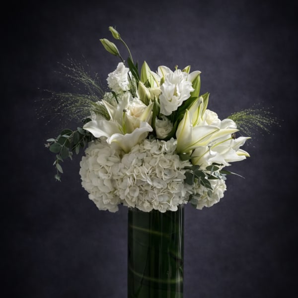 White lilies and hydrangeas arranged in a tall green vase