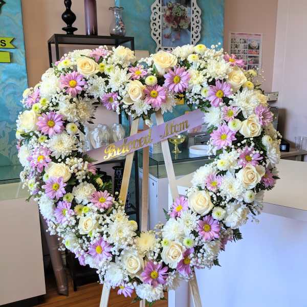 Heart-shaped floral wreath on an easel with a "Beloved Mom" ribbon