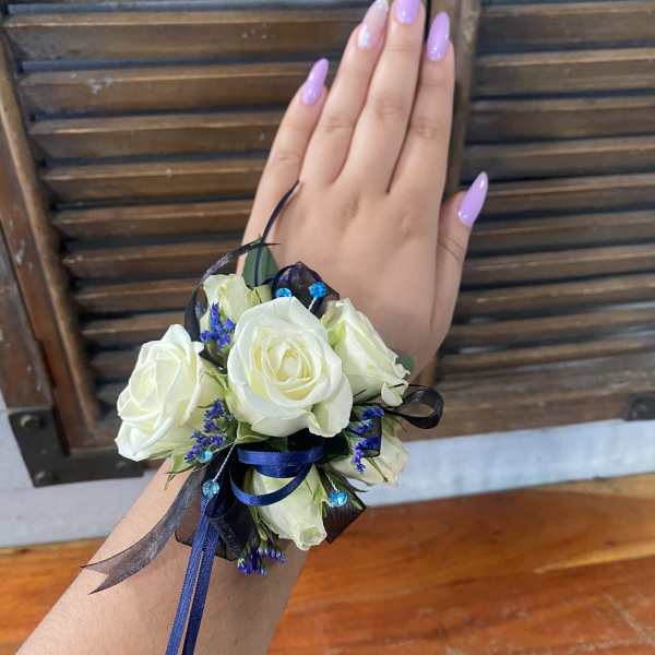 White rose wrist corsage with blue ribbon and small purple accents