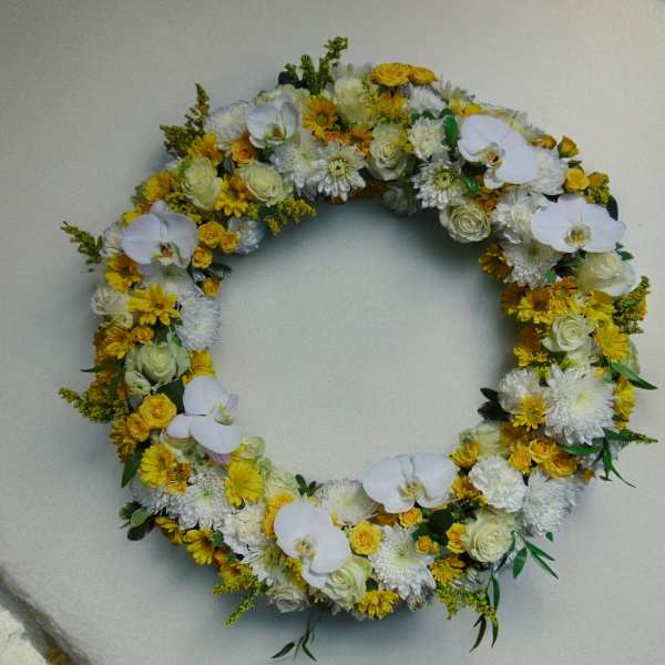 Large circular wreath of white orchids, roses, and yellow chrysanthemums arranged in a full ring