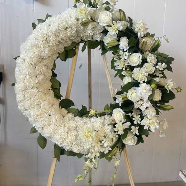 White floral wreath on a wooden easel with roses and lilies