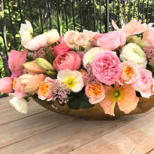 Low floral arrangement of pink and peach blooms in a gold bowl
