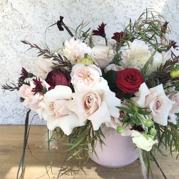 Mixed bouquet of pale roses and red blooms in a lavender vase