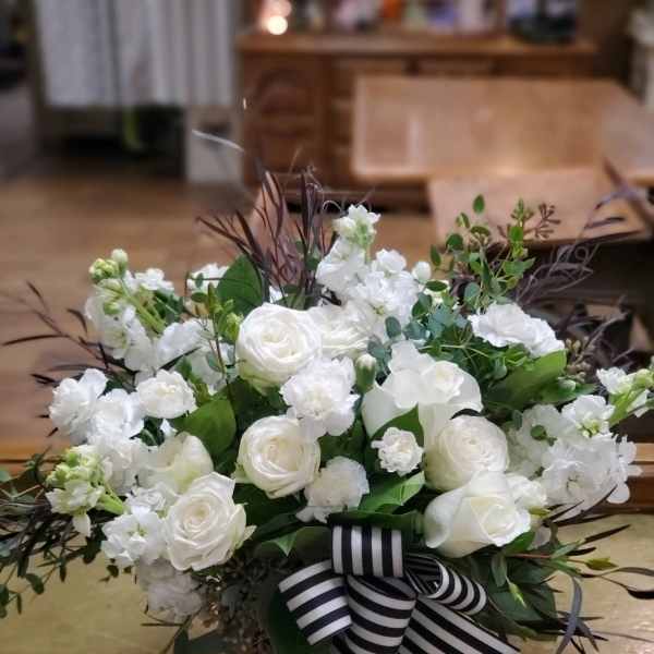 White floral arrangement with a striped ribbon in a low container