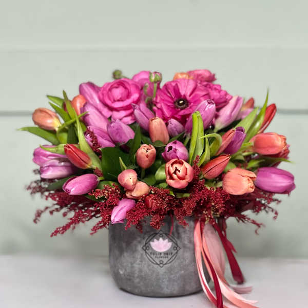 Pink and peach tulips arranged in a gray vase with ribbon