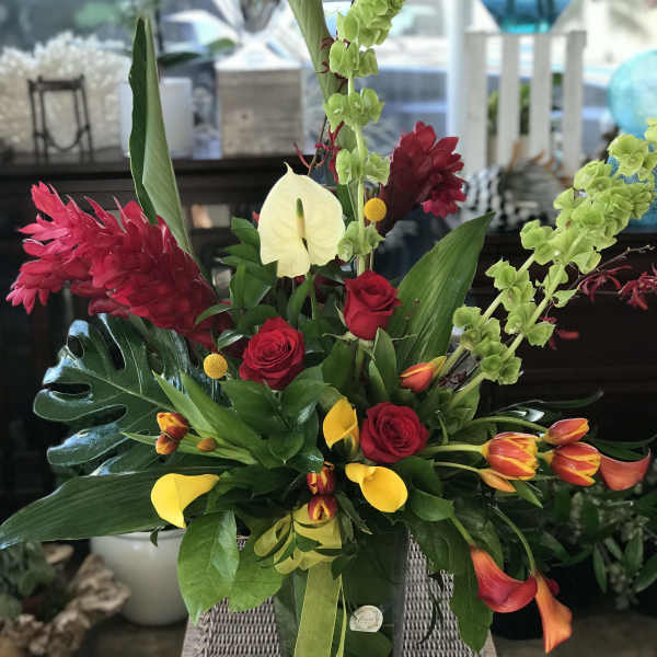 Tropical bouquet with red roses, yellow calla lilies, and green orchids in a glass vase